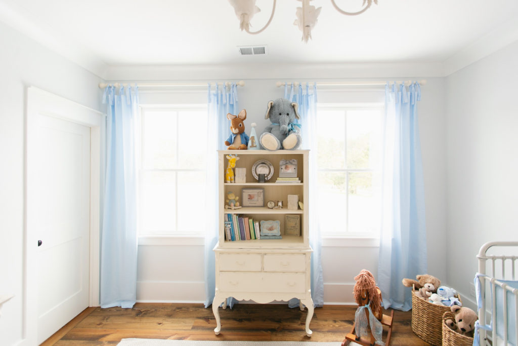 after photo of nursery showing blue tie-top curtains on two windows with a decorated chest in the middle 