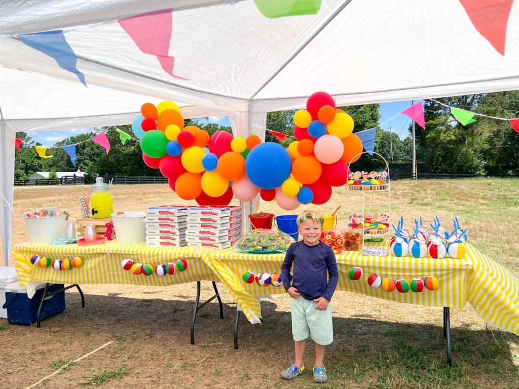 little boy smiling in front of the party table at his summer waterslide birthday party 