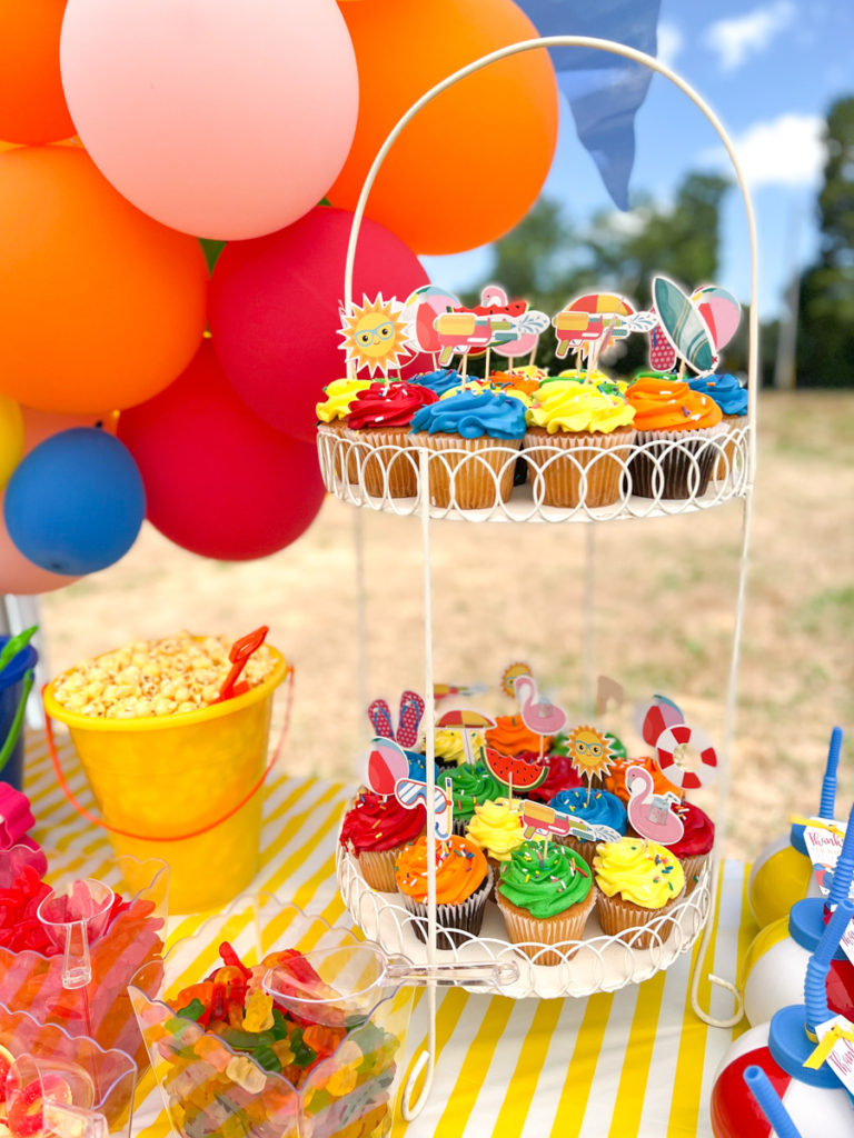 colorful cupcakes with summer themed cupcake toppers displayed in a cupcake stand at a summer waterslide birthday party 