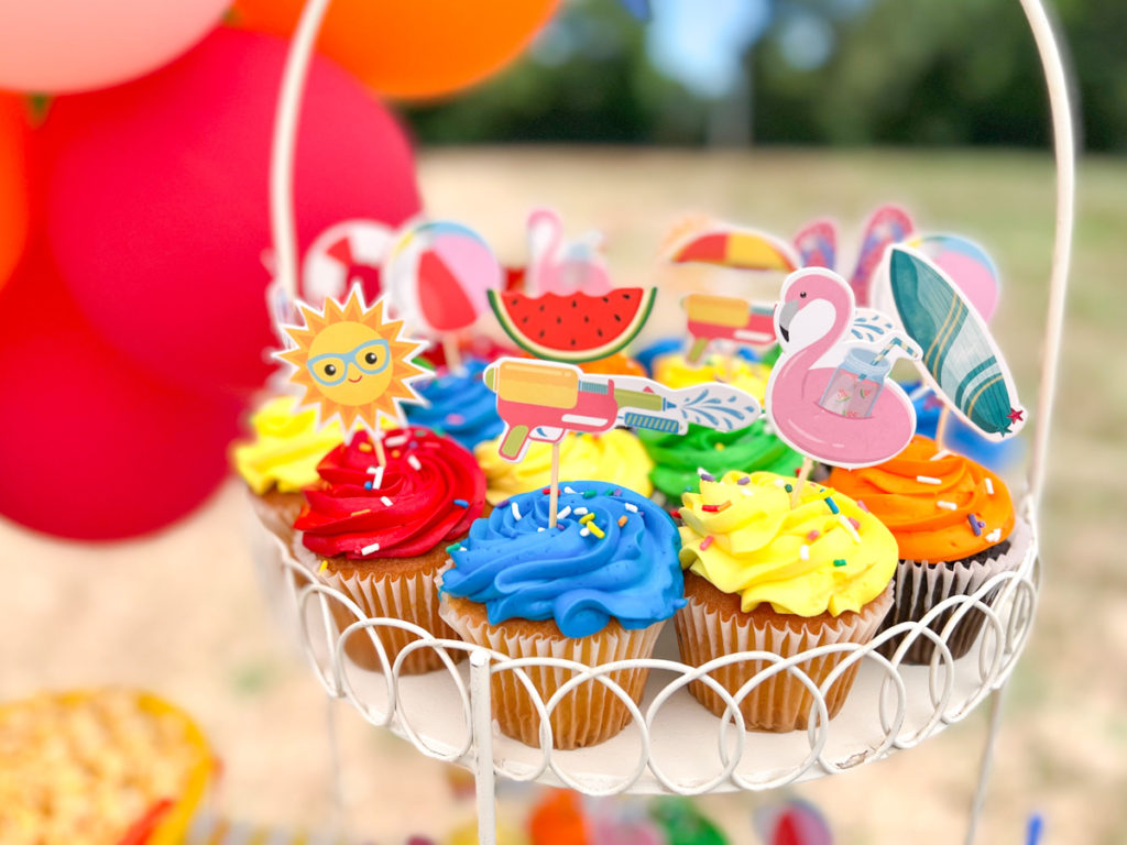 colorful cupcakes with summer themed cupcake toppers displayed in a cupcake stand at a summer waterslide birthday party 