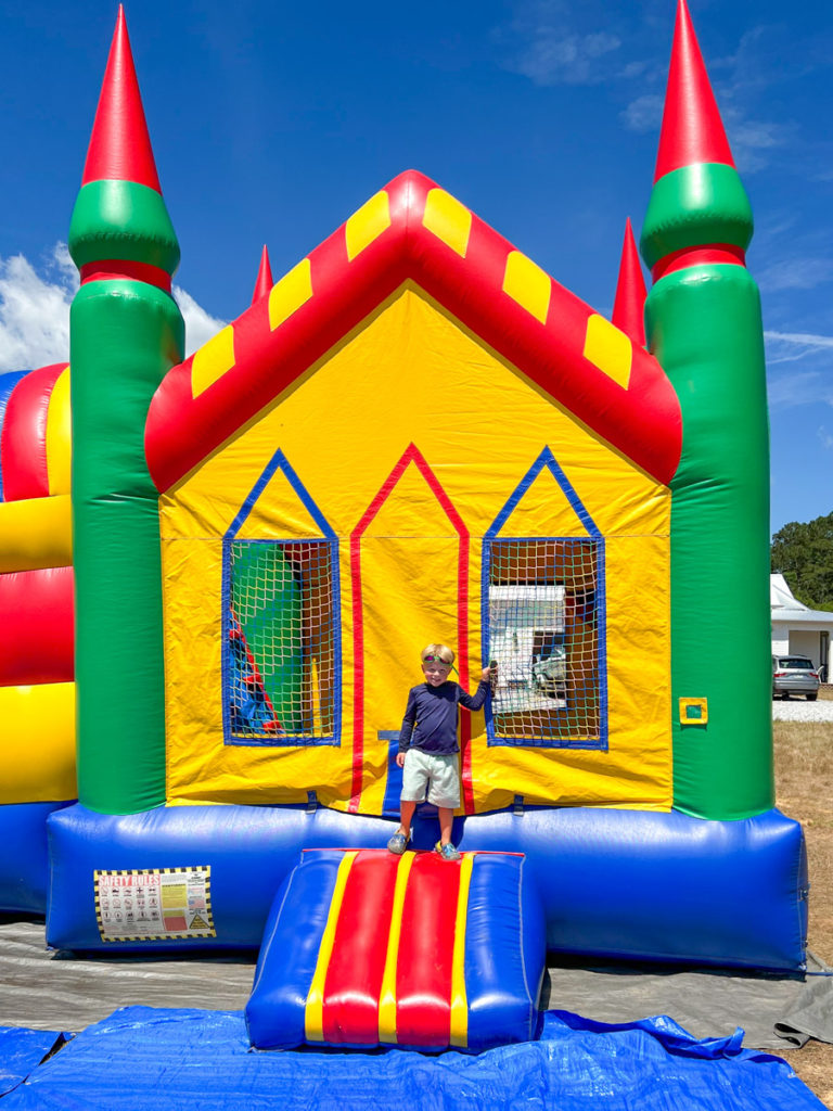 a little boy standing in front of a bounce house at his birthday party 