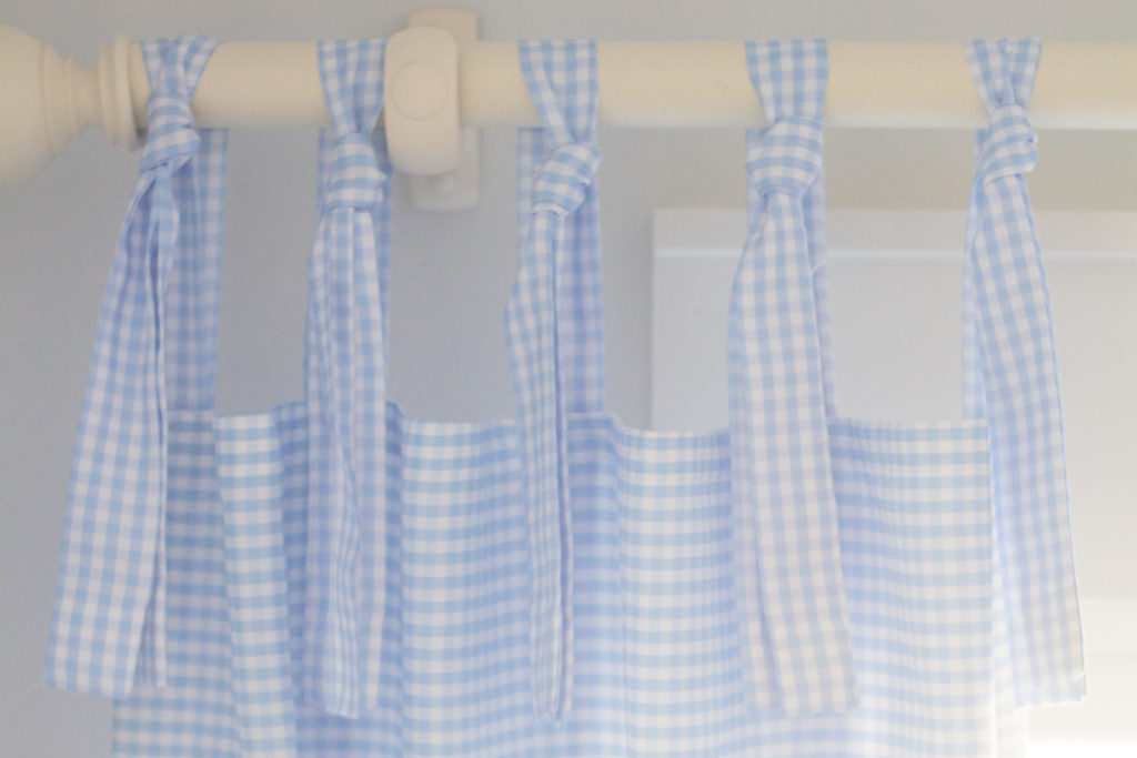 blue and white gingham tie-top curtains hanging on a curtain rod 