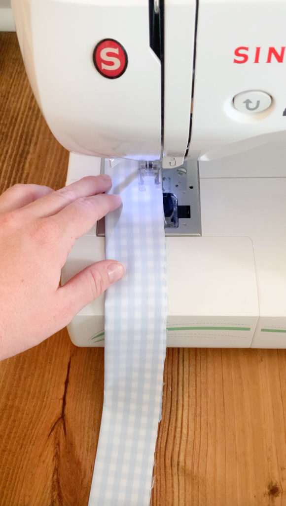 a photo showing a hand guiding a piece of fabric through a sewing machine 
