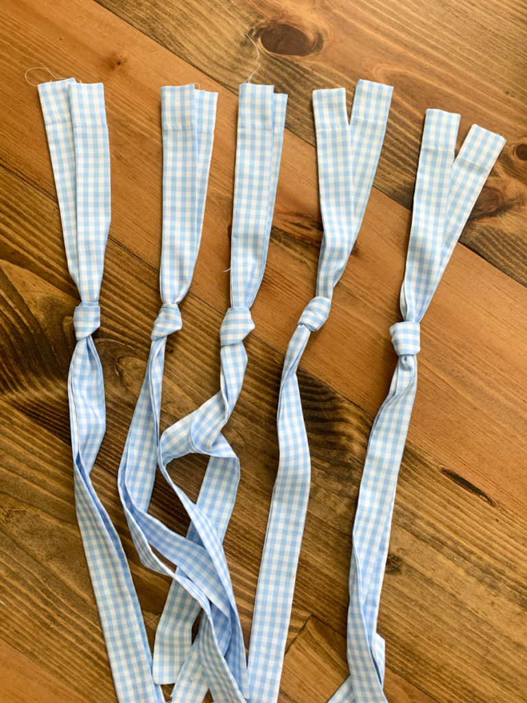 5 knotted blue and white gingham fabric curtain ties laying on the ground 