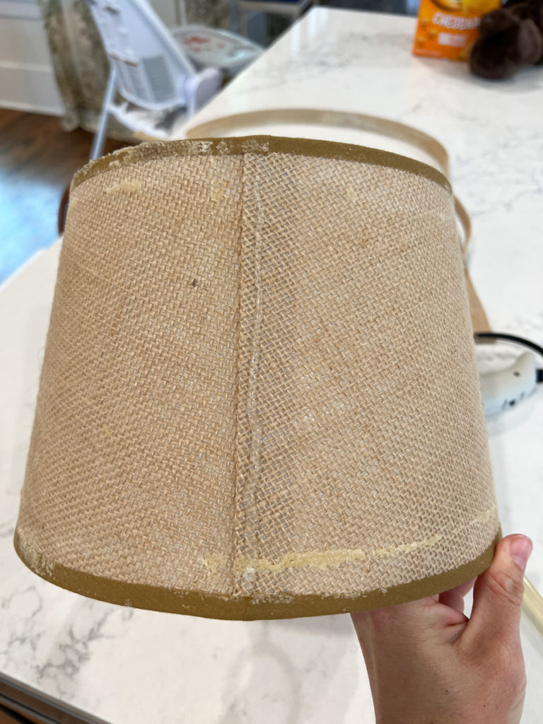 hot glue being applied to a lampshade to cover a lampshade with fabric for a diy craft project 