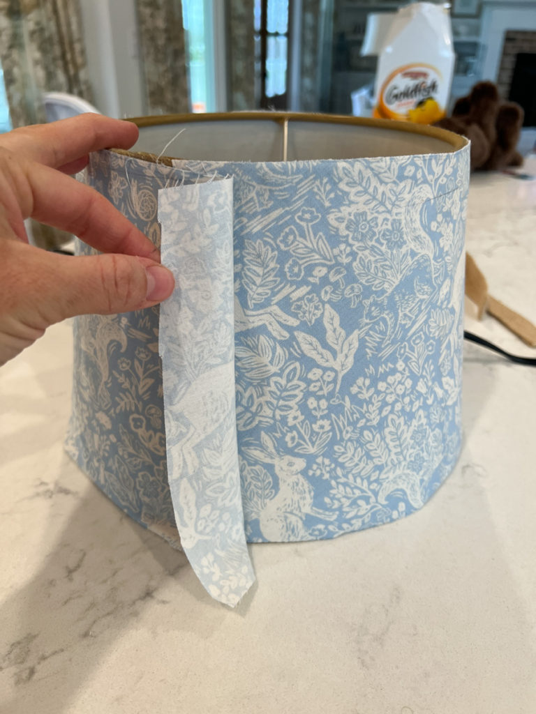 a lampshade being covered in fabric by gluing a piece of fabric to a lampshade 
