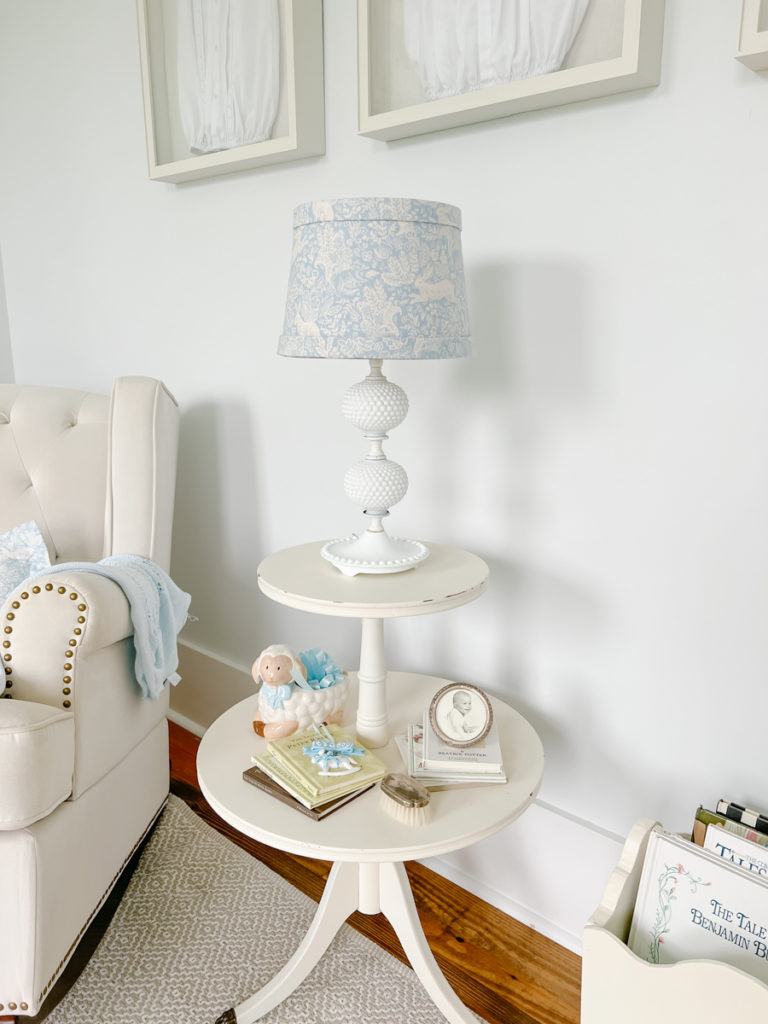 a fabric covered lampshade in blue and white bunny fabric on a lamp sitting on top of a white round side table in a blue and white nursery 