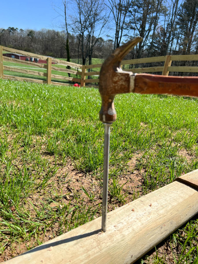 a hammer nailing a landscape spike through a landscape timber