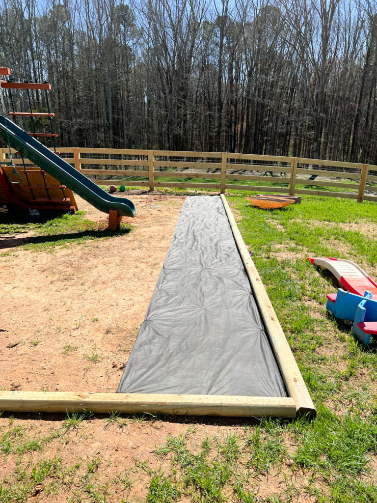 the first row of weed barrier landscape fabric rolled out inside the easy diy playground border
