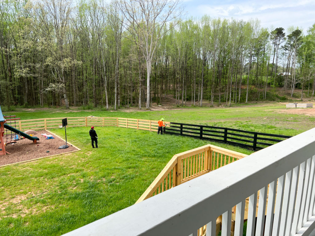 two men painting a horse fence black in the backyard 