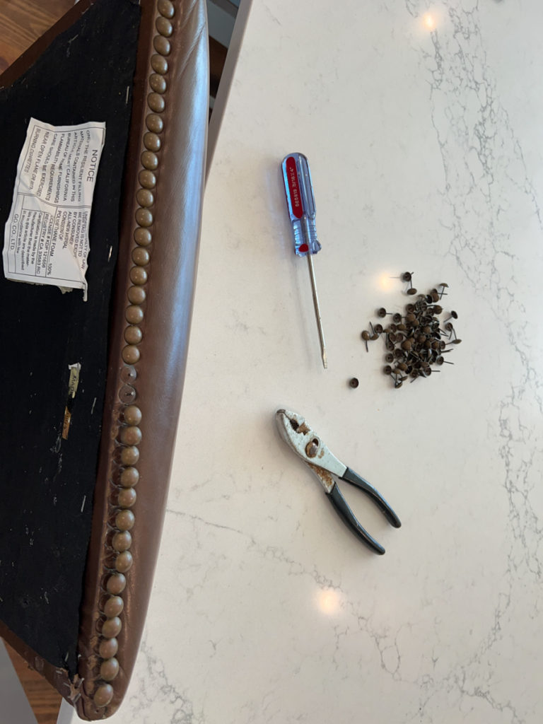 nailheads being removed from a barstool seat cushion with a screw driver and pliers 