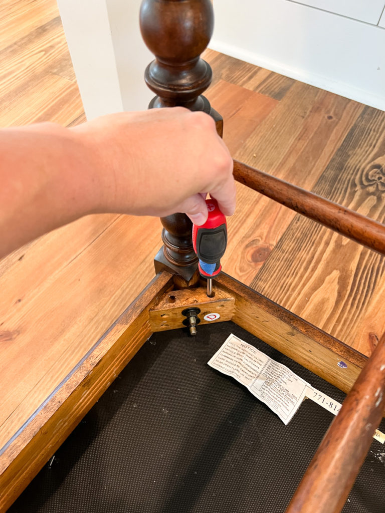 a hand turning a screw driver on the seat of a barstool cushion 