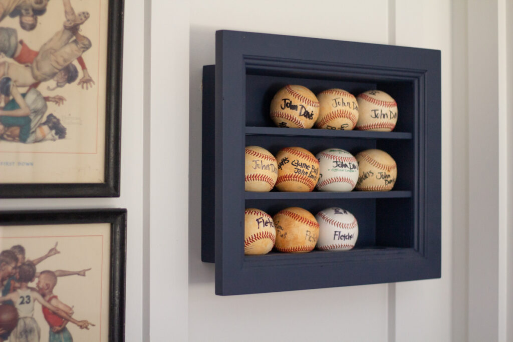 baseballs displayed in a baseball display base hanging on the wall in a shared boys bedroom 