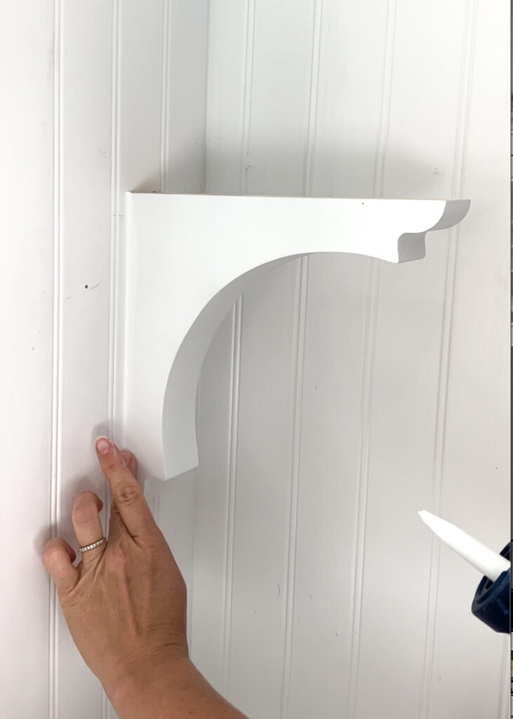 caulking a wood corbel that is hanging on the wall in a kitchen