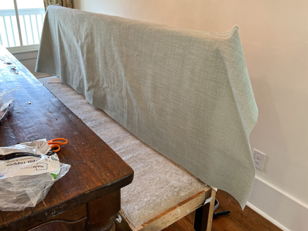 the construction process of a DIY banquette bench with batting and fabric stapled to the back 