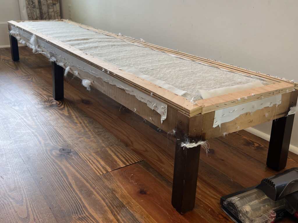 an upholstered bench with the fabric and batting removed revealing the wood frame of the bench 