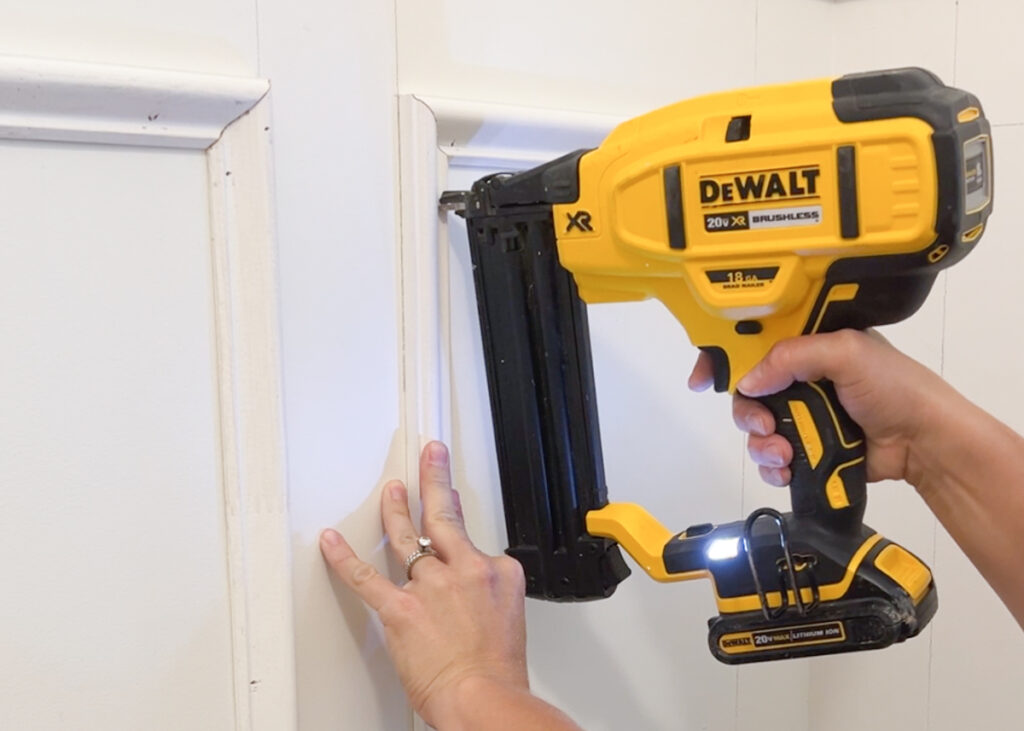 dewalt nailer nailing a piece of picture frame molding to the wall 