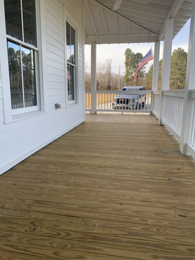 an unfinished wood porch floor installed on a white farmhouse before the porch floor was painted or stained